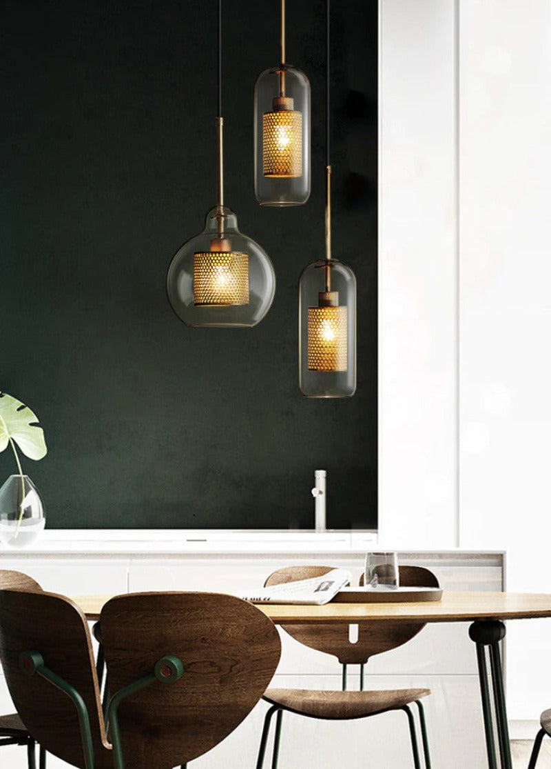 clear glass pendant lights with interior honeycomb shade in various shapes shown in brushed gold finish over kitchen table