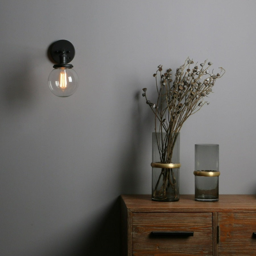 Vintage style wall sconce in black with clear glass globe shown on wall