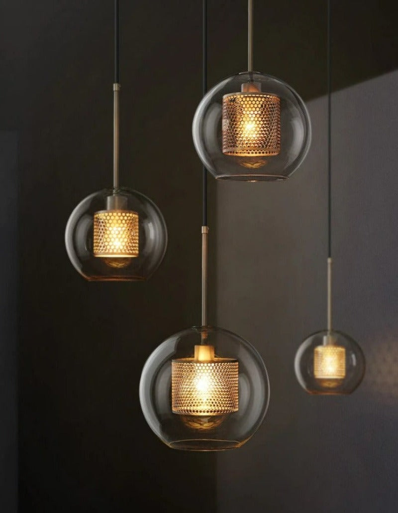 a grouping of clear glass globe pendant lights in small, medium and large with an interior honeycomb shade shown in brushed gold finish