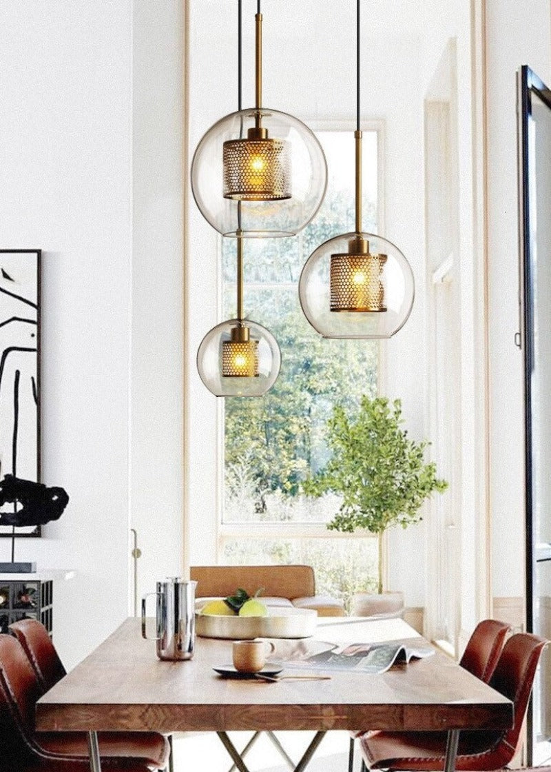 clear glass globe pendant lights with interior honeycomb shade shown in brushed gold finish over a dining table