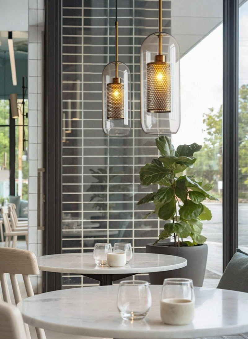 Oblong clear glass pendant lights with interior honeycomb shade shown in brushed gold finish shown hanging over a dining table